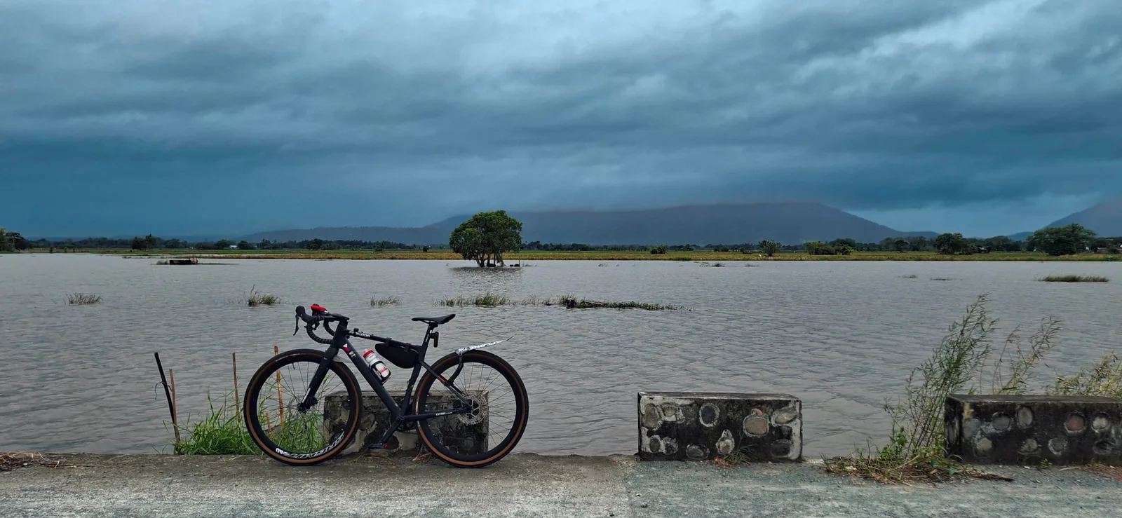 A bicycle beside water under storm clouds